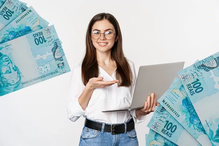 Mulher sorridente usando notebook, rodeada por notas de 100 reais, fundo branco