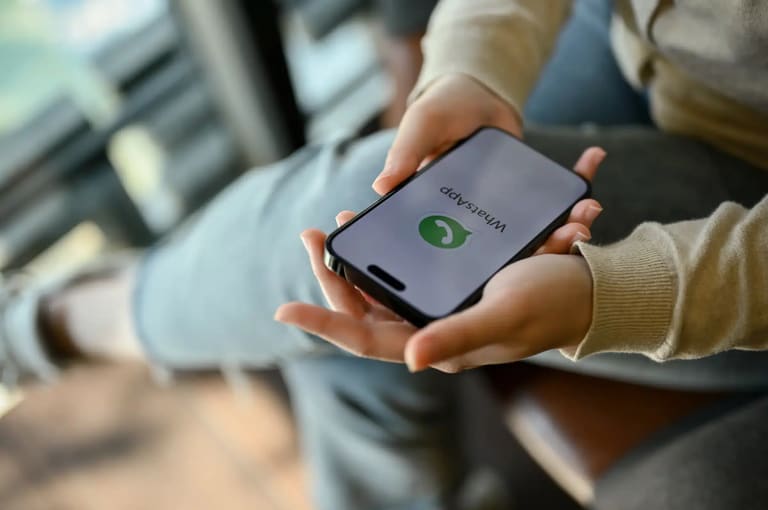 Pessoa segurando smartphone com WhatsApp aberto, ilustrando como evitar mensagens de listas de transmissão.
