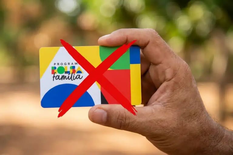 Mão segurando cartão do Bolsa Família com X vermelho, sinalizando cortes.