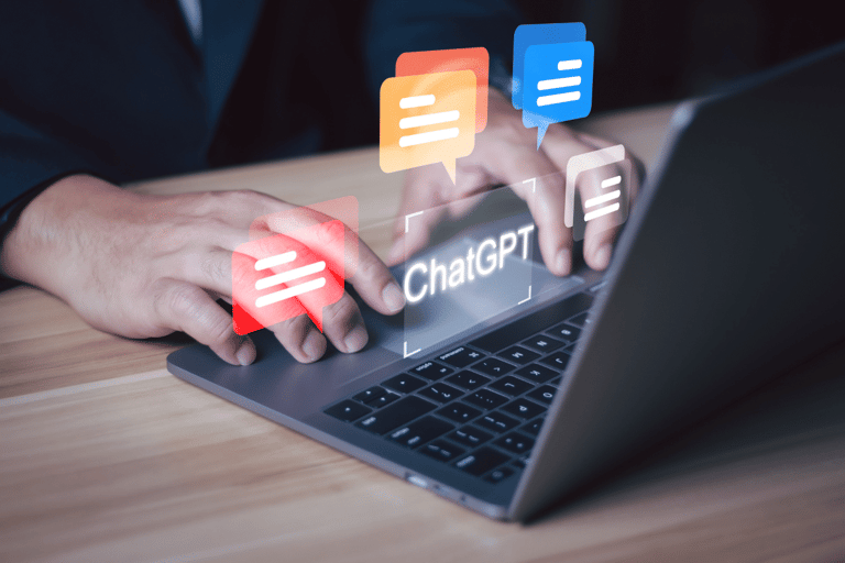 Pessoa digitando em laptop cinza com balões de conversa coloridos e texto "ChatGPT" na tela