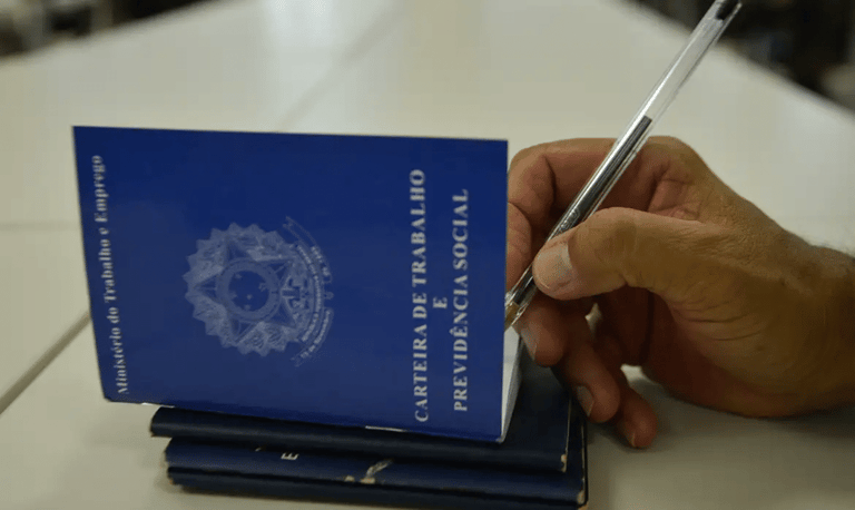 Cargos CLT maiores salários - mão segurando caneta sobre Carteira de Trabalho e Previdência Social azul