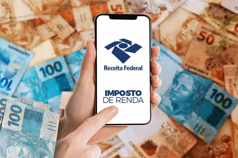 Mão segurando smartphone com logo da Receita Federal e texto "Imposto de Renda" sobre notas de real