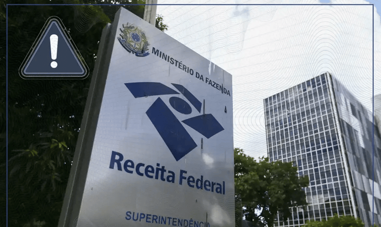 Placa de identificação da Superintendência da Receita Federal do Ministério da Fazenda em frente a edifício comercial, com ícone de alerta amarelo em destaque