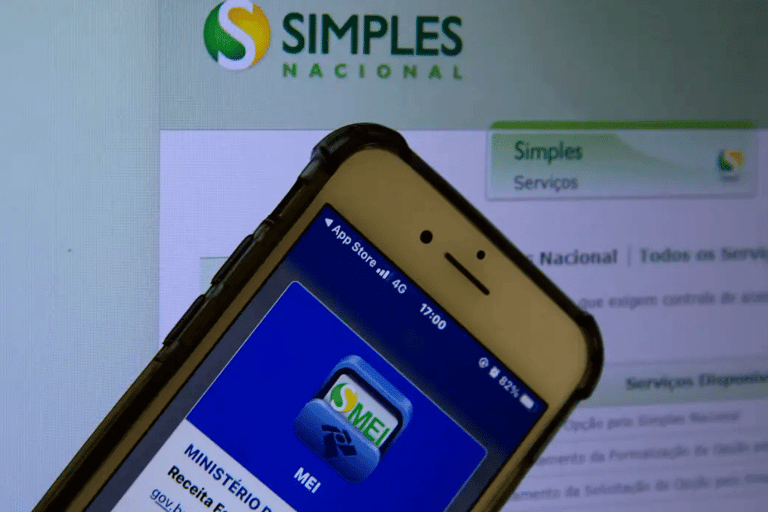 Smartphone com app MEI aberto na tela sobre monitor exibindo Portal do Simples Nacional