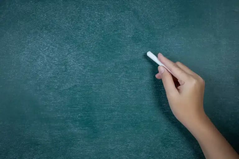 Uma mão escrevendo em um quadro-negro, simbolizando o direito dos professores temporários ao piso nacional, conforme decisão do STF.