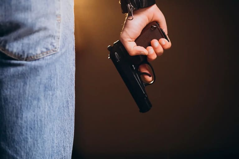 Pessoa segurando arma de fogo ao lado do corpo, representando profissões com autorização de porte no Brasil.