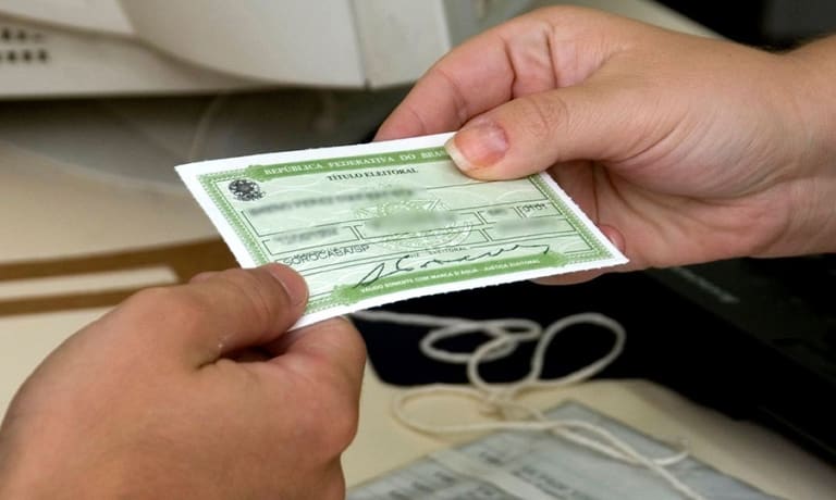 Pessoa segurando o título de eleitor brasileiro com informações visíveis no documento.