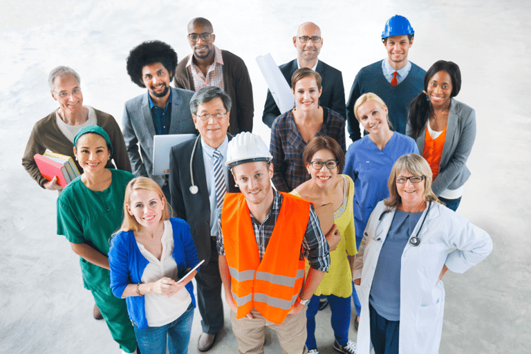 Grupo de 14 pessoas com roupas profissionais variadas, incluindo médicos, engenheiros, enfermeiros e executivos, olhando para cima e sorrindo