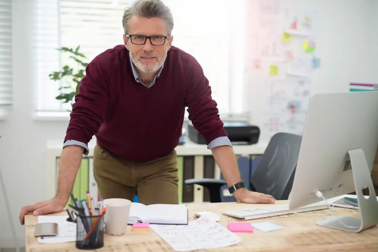 Profissional experiente com mais de 50 anos trabalhando em escritório moderno e demonstrando liderança no ambiente corporativo.