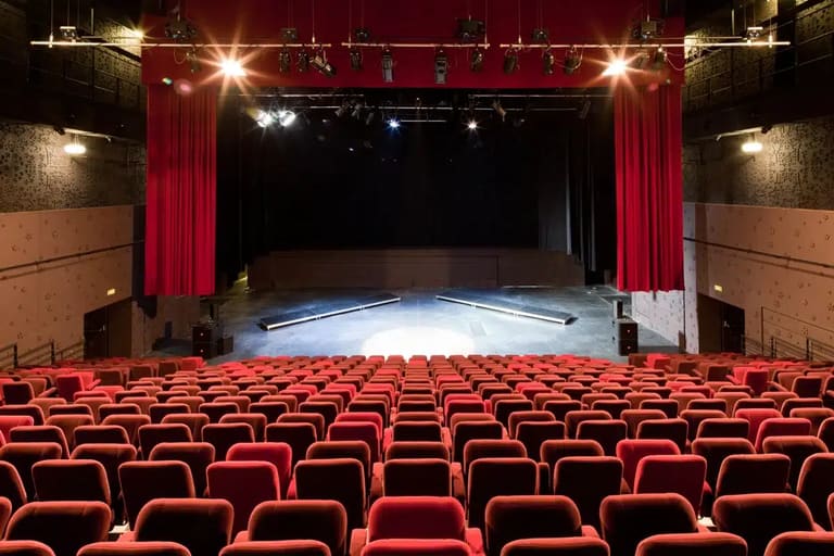 Palco de um teatro, com cadeiras vermelhas e luzes direcionadas ao palco, representando os caminhos profissionais no universo teatral.