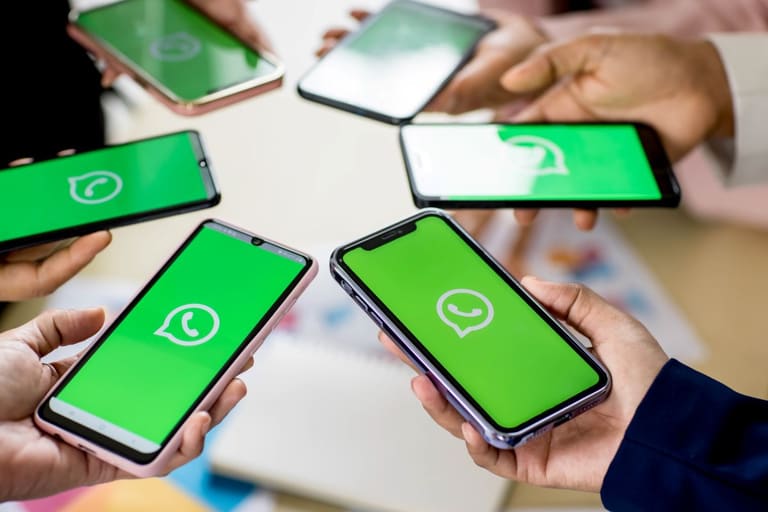 Várias pessoas segurando smartphones com o logo do WhatsApp na tela, representando a possibilidade de usar a mesma conta em múltiplos dispositivos.