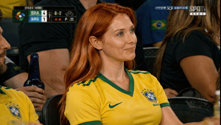 Mulher sorrindo sentada em arquibancada de jogo de futebol.