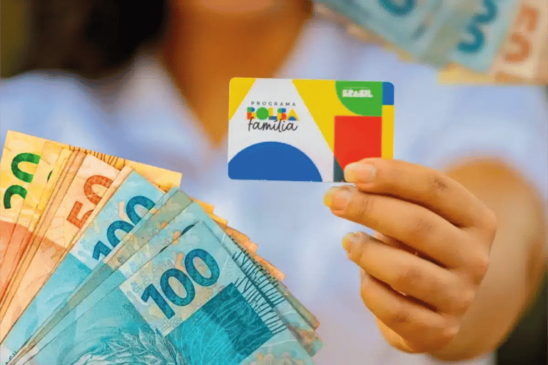Pessoa segura cartão do Bolsa Família e cédulas de dinheiro representando o pagamento do benefício de maio.