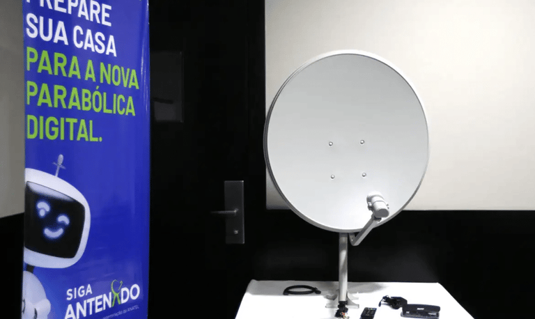 Kit da nova parabólica digital exposto ao lado do banner da campanha Siga Antenado da Anatel sobre a troca de antenas