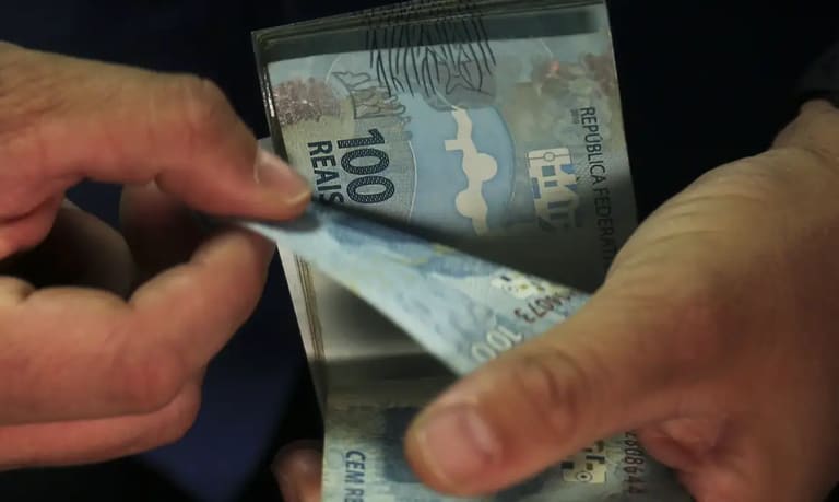 Mãos contando notas de cem reais durante recebimento de valores do abono salarial PIS/Pasep