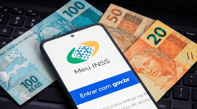 Smartphone exibindo tela do Meu INSS com botão gov.br sobre notas de 100, 50 e 20 reais em teclado preto.