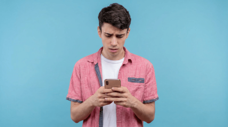 Jovem confuso olhando celular com expressão preocupada.