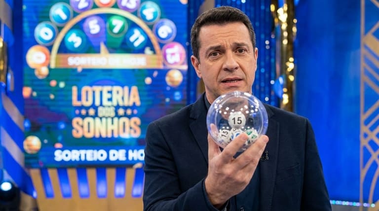 Homem de terno segura globo transparente com bola número 15 em estúdio da Loteria dos Sonhos