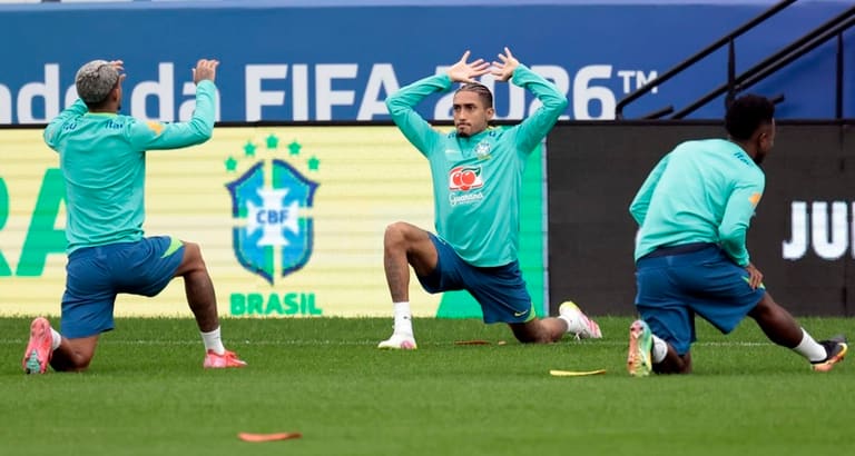Jogadores da seleção brasileira fazem alongamento em treino diante de painel da Copa do Mundo FIFA 2026