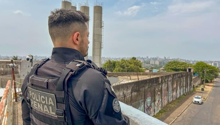 Agente da Polícia Penal de costas observa muro de unidade prisional