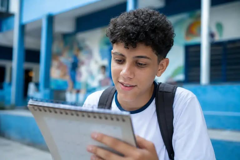 Estudante brasileiro em uniforme escolar olhando para um calendário, representando a consulta às datas de pagamento do programa em junho de 2026.